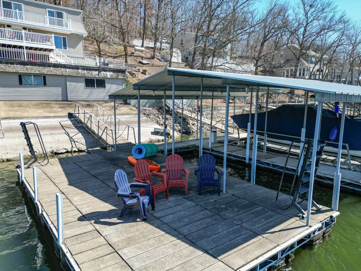 A set of colorful Adirondack chairs sits on a boat dock over calm water, surrounded by trees. The space invites lounging, sunbathing, fishing, or sharing stories by the water at sunset.