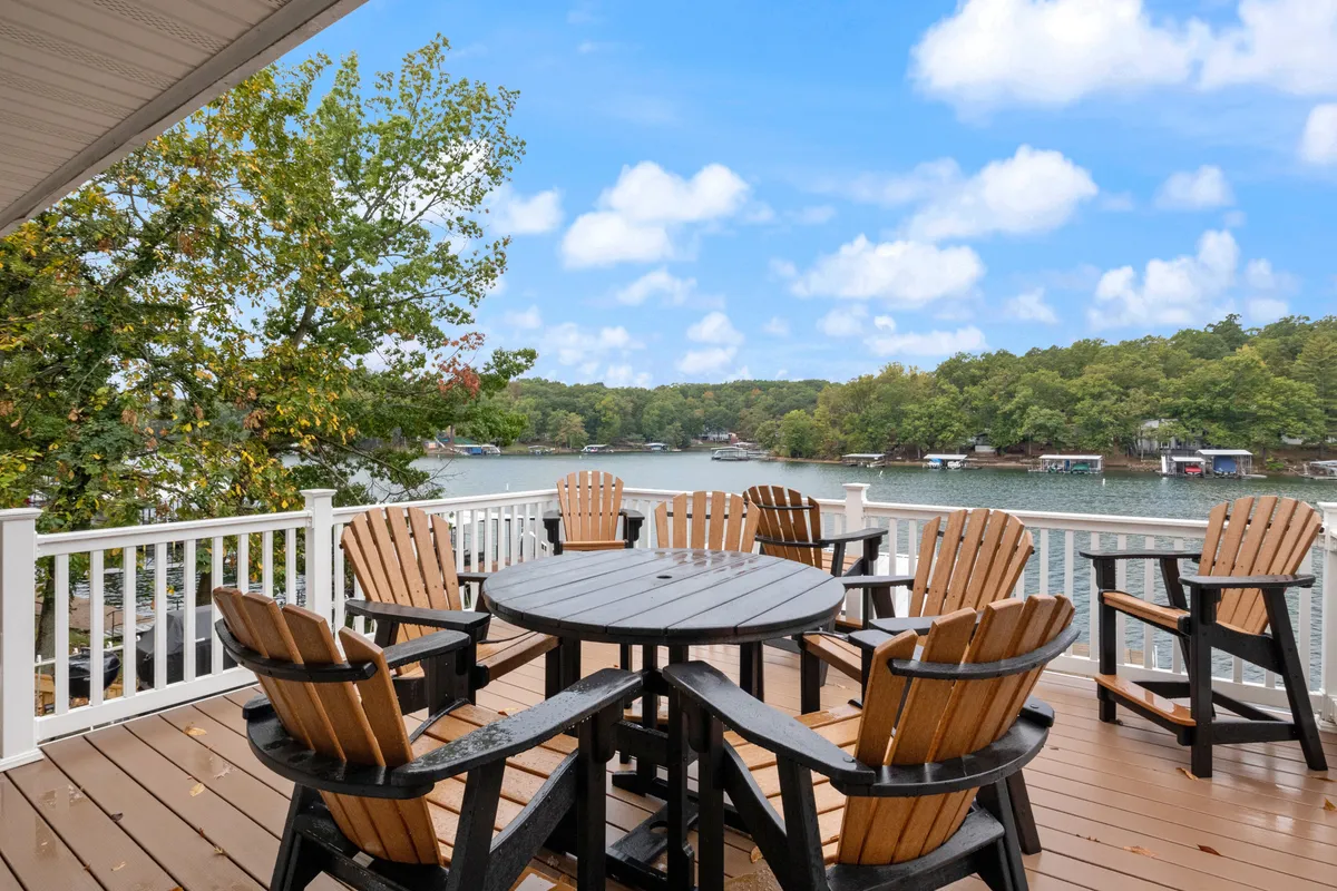An inviting outdoor deck featuring a circular table surrounded by Adirondack chairs, overlooking the lake and nestled amongst trees. The scene captures the relaxed mood of outdoor dining or evening conversations while enjoying the natural surroundings.