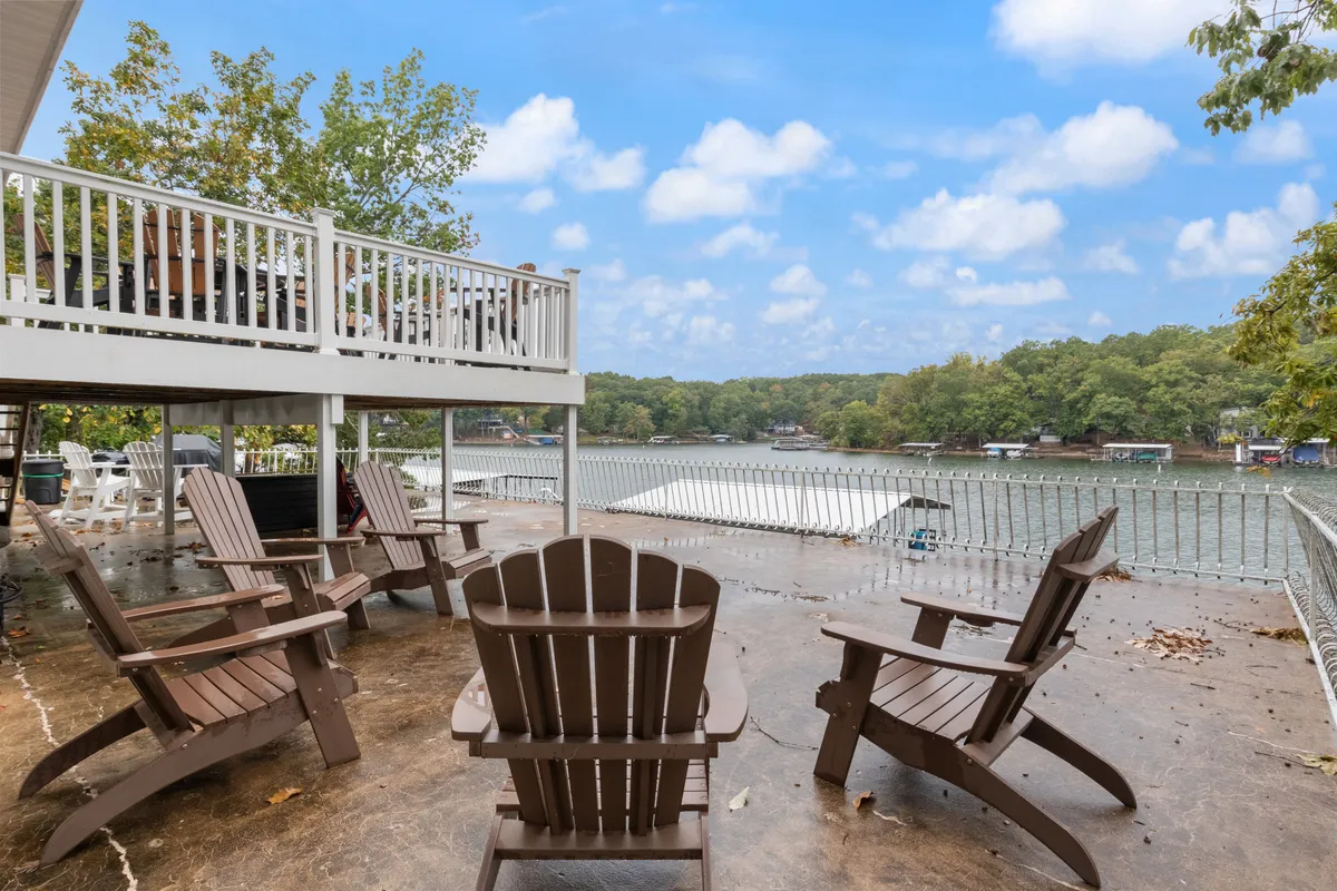 This image shows a spacious deck with Adirondack chairs overlooking a tranquil lake, framed by a sturdy deck railing and surrounded by lush greenery. The arrangement suggests a welcoming, communal outdoor space ideal for gatherings and sunset conversations.