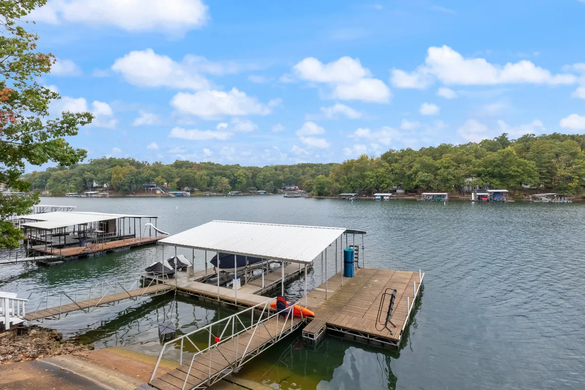 The hero image captures a tranquil lakeside view with inviting boathouses and docks stretching out over calm, shimmering water, framed by lush, leafy trees. The scene evokes a relaxed mood and hints at activities like boating, fishing, swimming, and picnicking, with the deck and dock areas prominently featured for lakeside leisure. The golden hour light enhances the serenity and warmth of the setting.