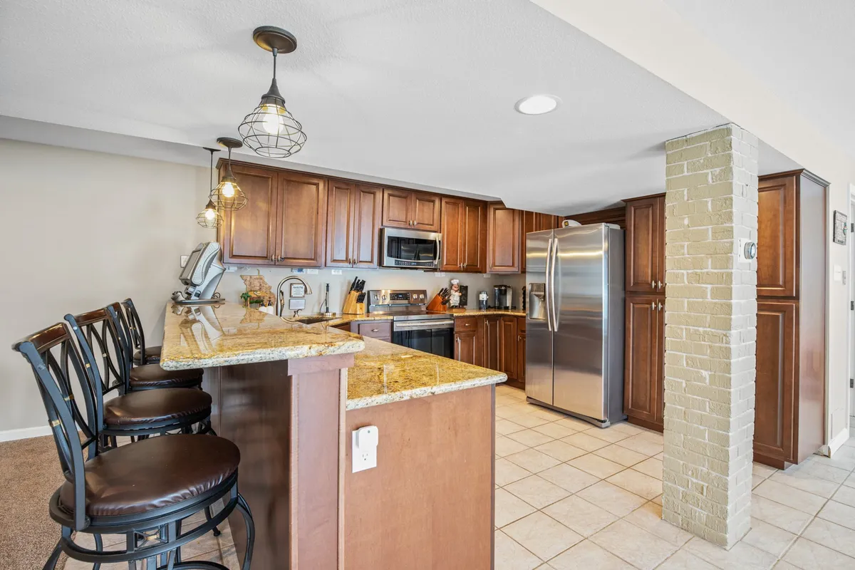 A stylish kitchen with granite countertops, wooden cabinetry, modern stainless steel appliances, and bar stools for casual seating. The space looks ready for cooking, entertaining, or simply gathering for coffee and conversation.