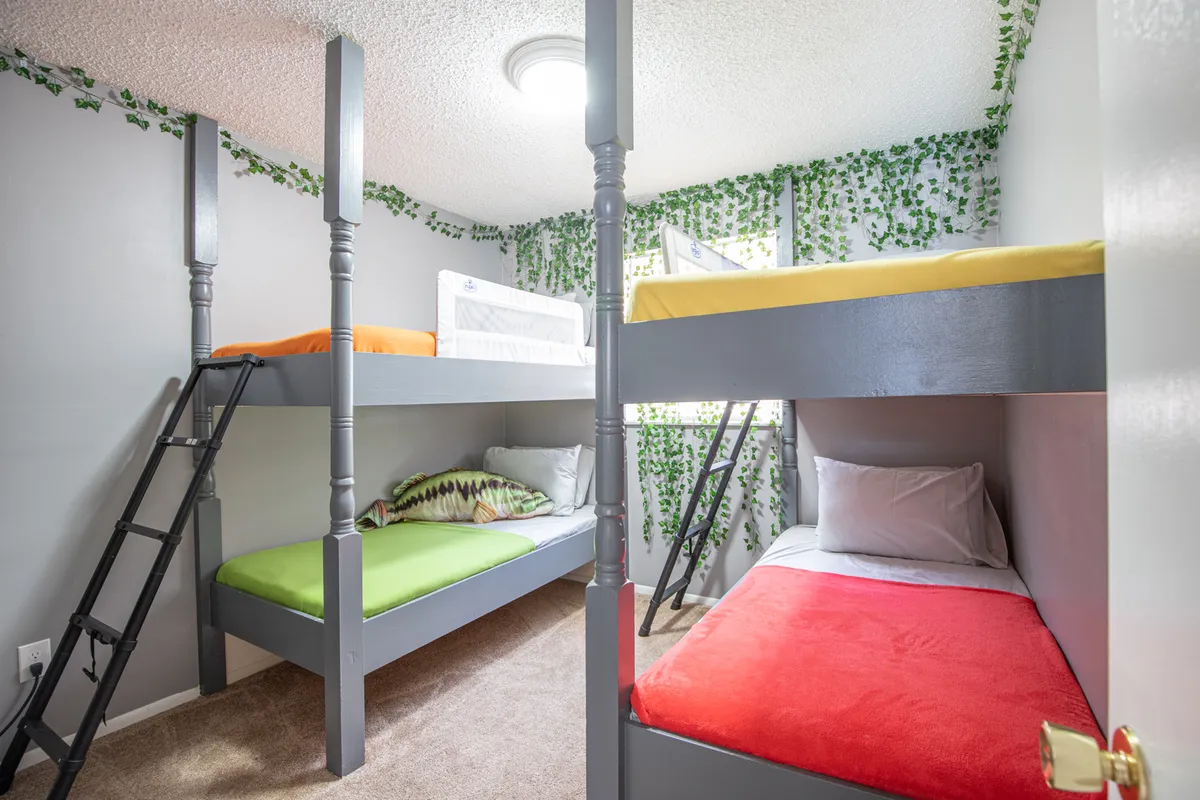 A fun and cozy bunk room with colorful bedding, whimsical greenery on the walls, and an inviting ambiance. The setup encourages storytelling, play, and shared experiences.