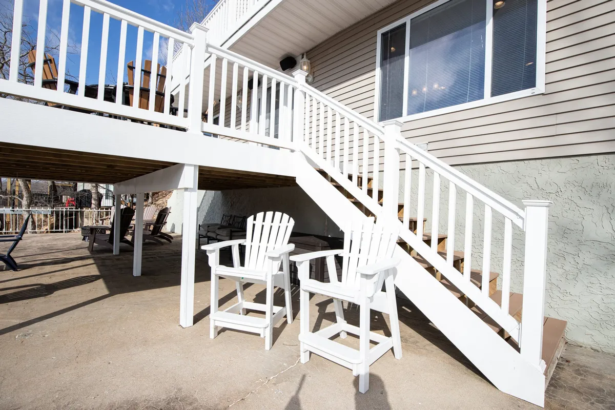 An inviting exterior patio area featuring white Adirondack chairs and a staircase leading down to the yard, suggesting a comfortable transition from indoor spaces to the outdoors. The patio looks out toward the surrounding nature, ideal for relaxation after adventures on the lake.