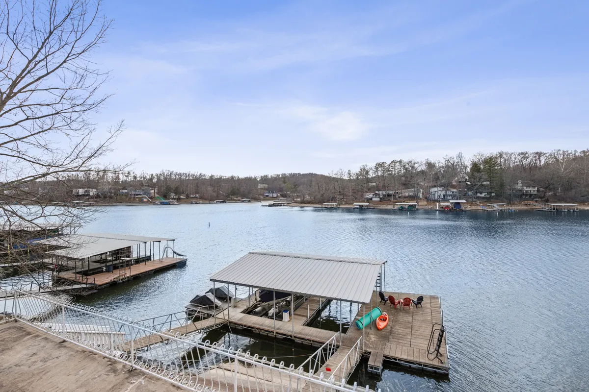 A sweeping view of the lake, private docks, boathouses, and lush tree line. The dock is shown invitingly, with calm water and a sense of tranquility, suggesting easy access for boating and fishing excursions.